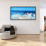 Modern beach oil painting on canvas with rich impasto texture hanging in a modern living room with a beige sofa, showing full room decor.