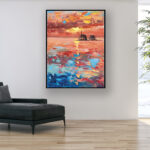 Vibrant sunset beach oil painting on canvas with rich impasto texture hanging in a modern living room with a black sofa, showing full room decor.